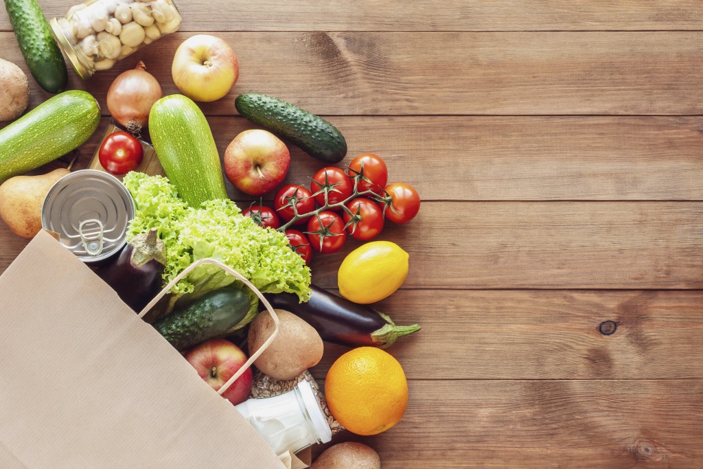 Paper grocery bag with fresh vegetables, fruits, milk and canned goods on wooden backdrop. Food delivery, shopping, donation concept. Healthy food background. Flat lay, copy space. Credit, Candle Photo, iStock. 