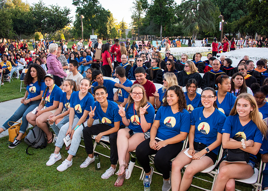 A group of students sit on chairs on the library lawn during New Student Convocation.