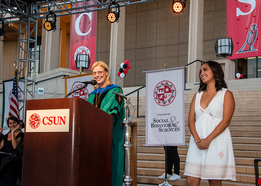 CSUN President Dianne F. Harrison at a podium while a female CSUN student stands nearby on stage.