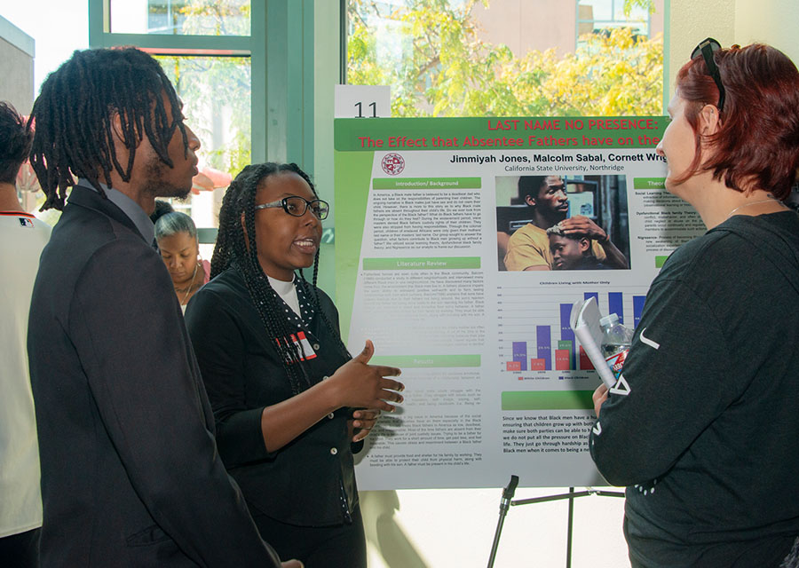 Jimmiyah Jones and Malcolm Sabal stand by their poster, explaining it to an attendee.