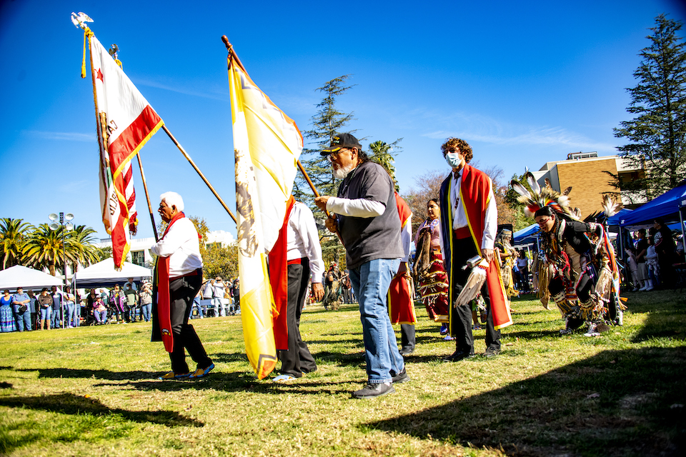 Attendees process across the lawn near the Sierra Quad carrying flags.