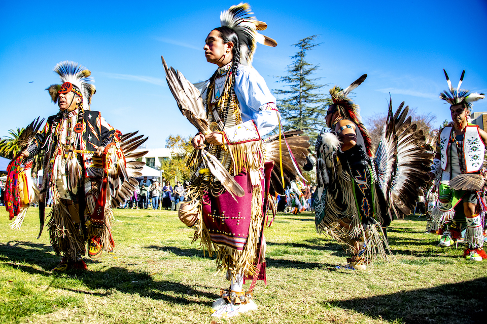 Attendees process across the lawn wearing Native American regalia.