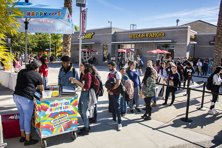 A long line of students form in front of a shaved ice cart for free shaved ice.