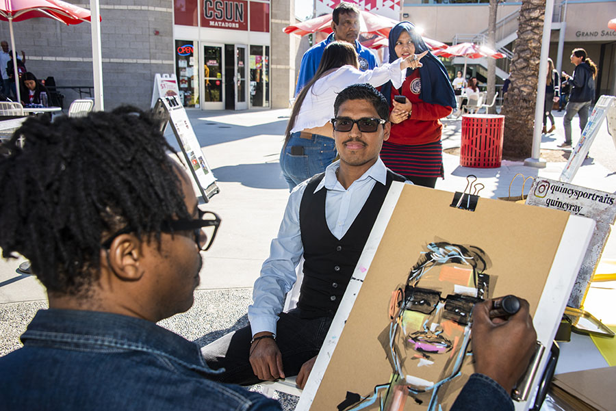 A caricature artist draws a portrait of a smiling student with sunglasses.