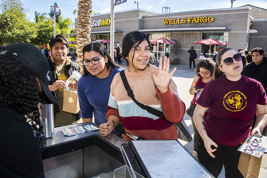 A smiling female student waves at the camera as she waits for her free shaved ice.