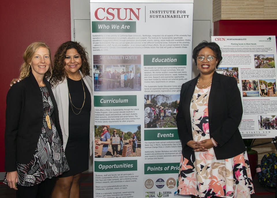 Erica Wohldmann, Francesca Vega, and Stephanie Wiggins stand by a poster about the Institute for Sustainability.
