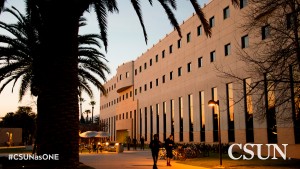 Two people walk in front of Bookstein Hall, framed by palm trees, as the sun sets.